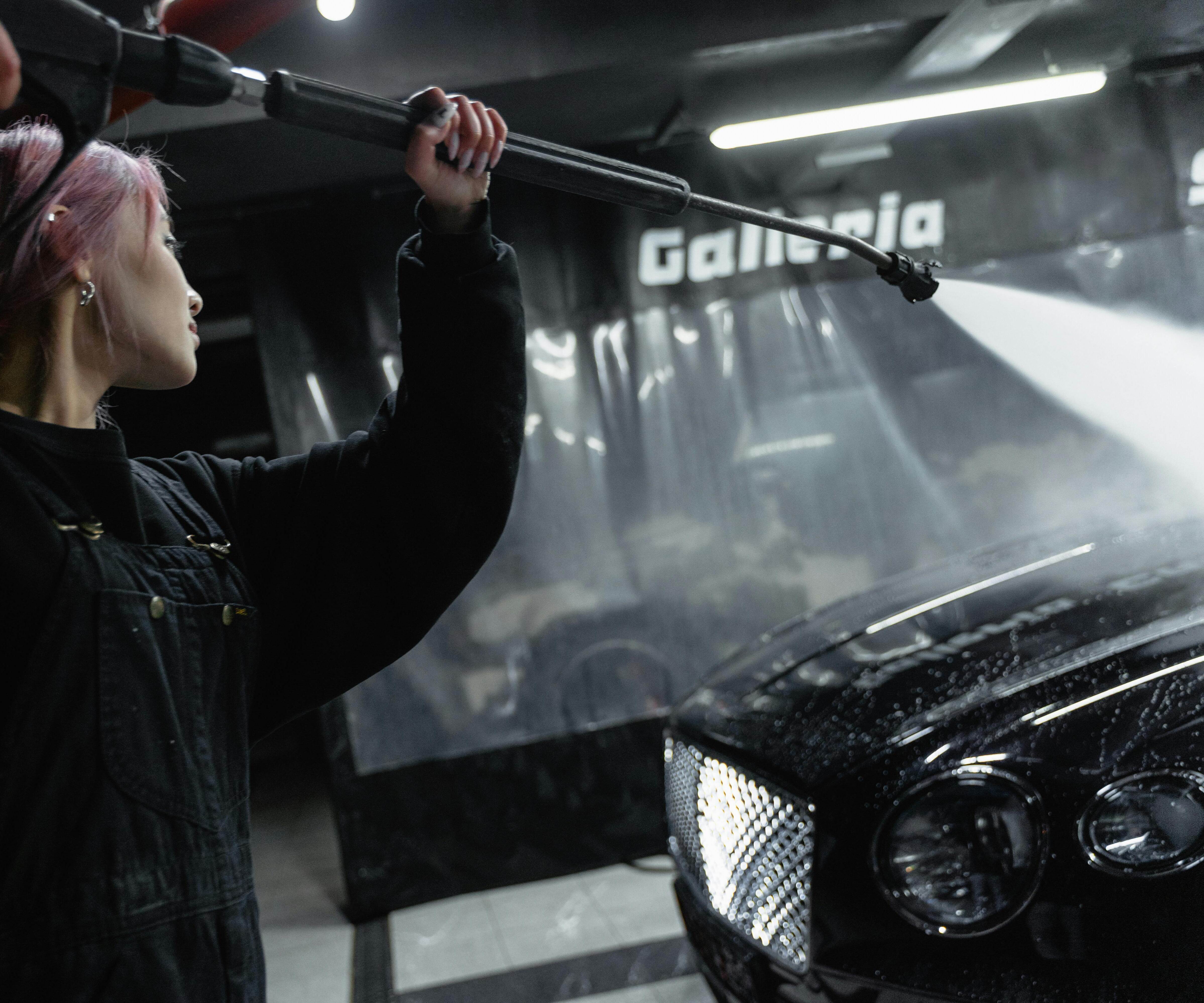 A woman using a pressure washer to clean the exterior of a car, removing dirt and grime before detailing.